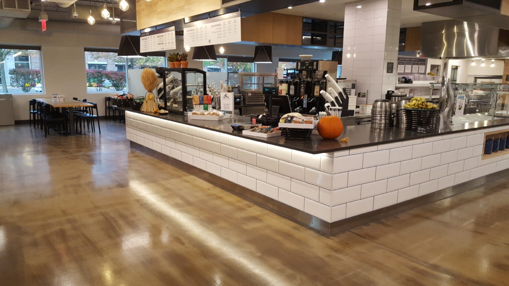 A wood-like stained urethane floor in a food hall setting with tables and white tiled service areas.