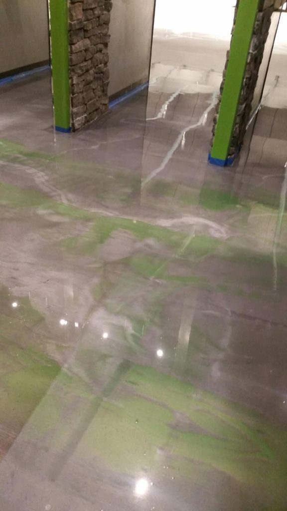 A glossy metallic epoxy floor with green swirls that match nearby wall features