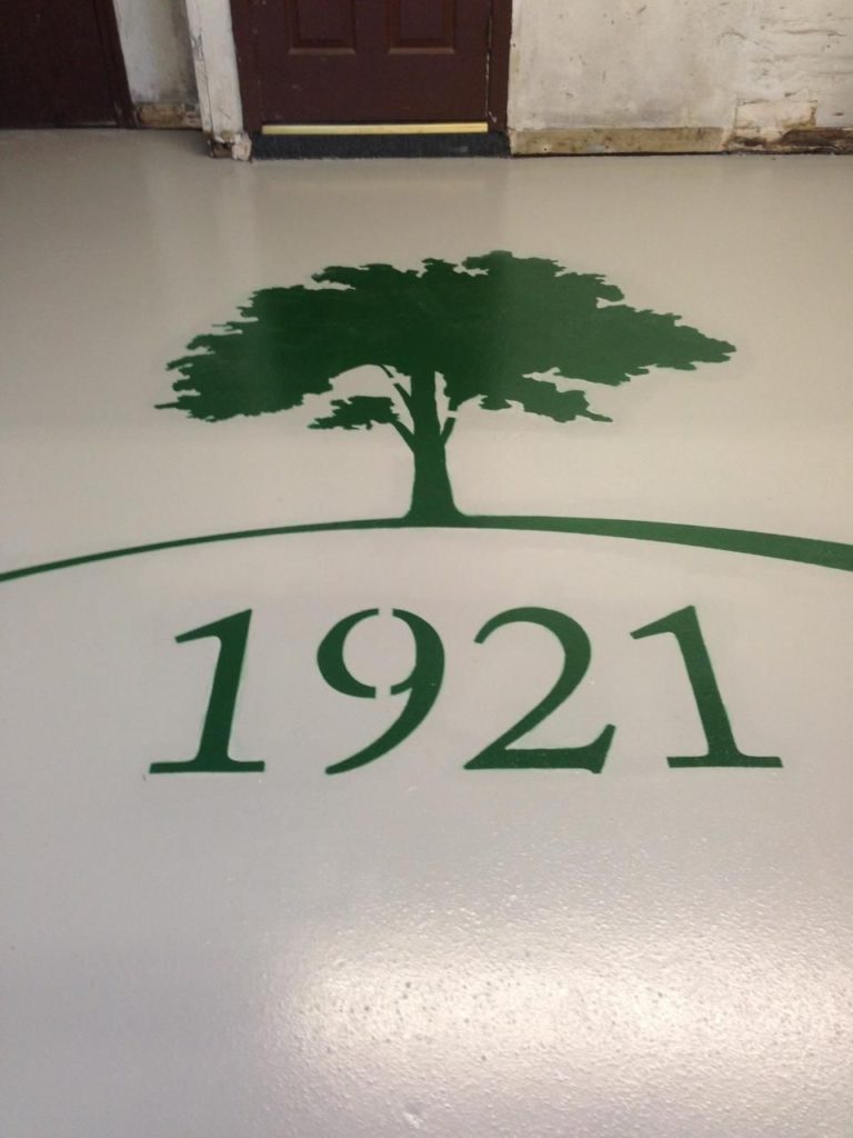 A solid white epoxy floor in a maintenance shop bears a giant green tree logo and the year 1921.