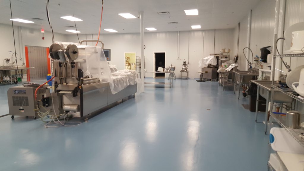 Pale blue epoxy flooring in a food and beverage manufacturing facility surrounded by machinery and industrial sinks.
