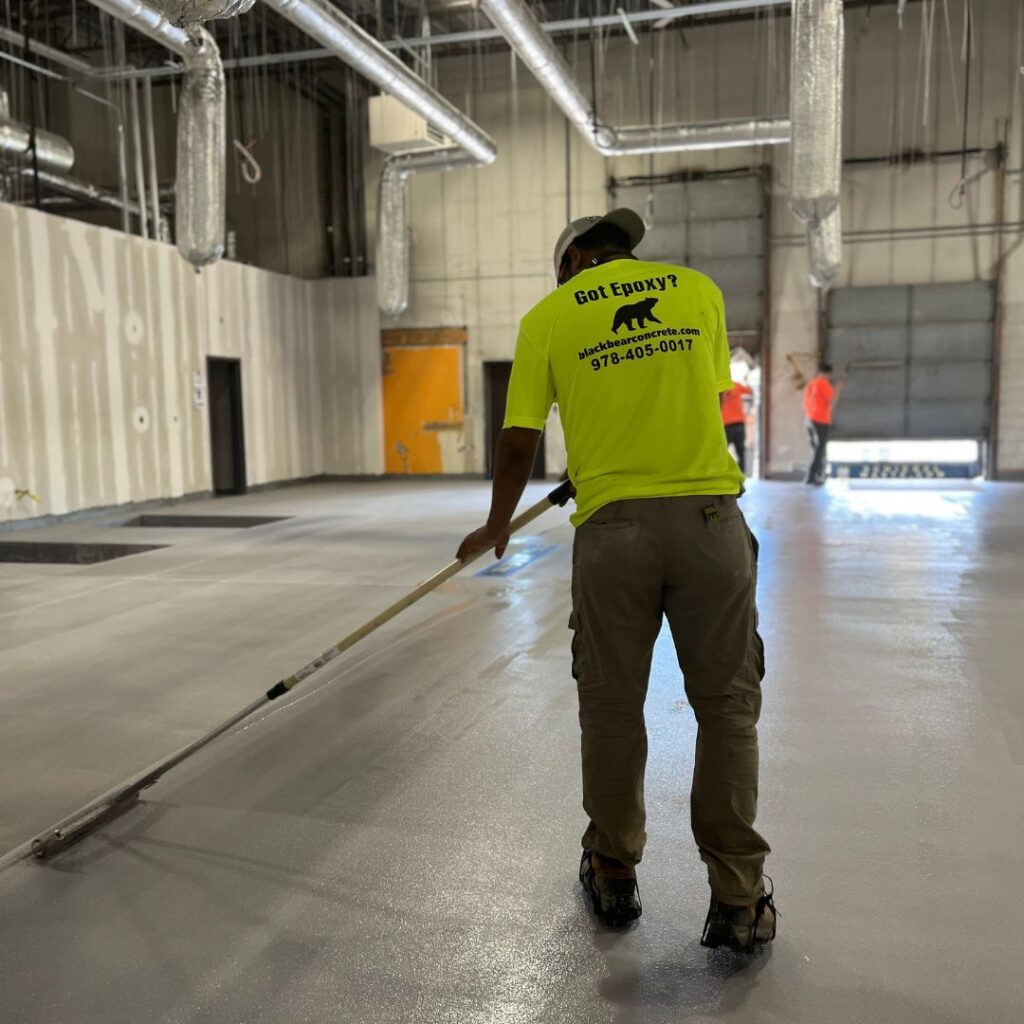 A Black Bear contractor works on a gray resin flooring project in a large warehouse